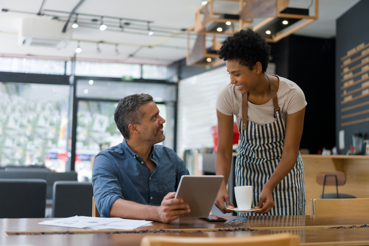 Happy African American waitress serving coffee to a man working at a cafe and smiling - food and drink establishment concepts