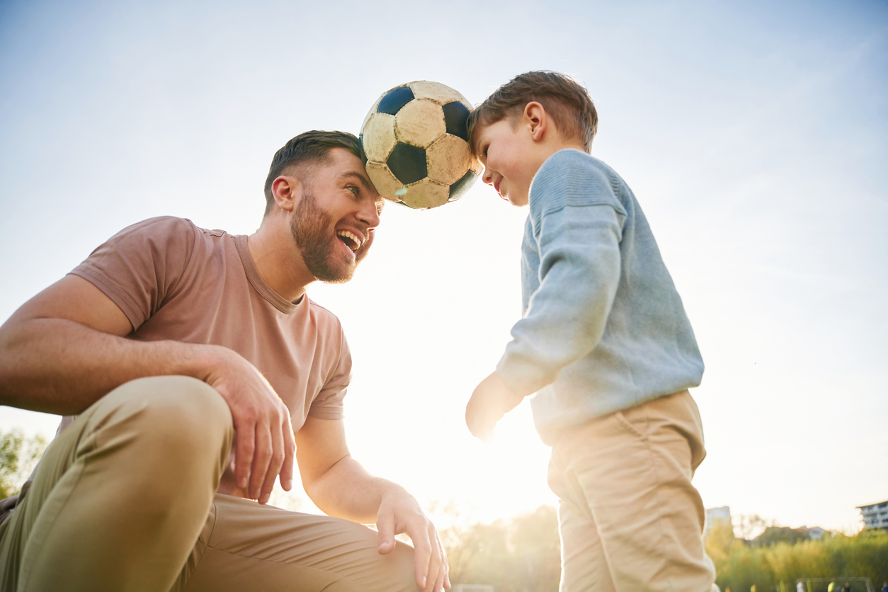 Soccer ball, holding it by heads, fun. Happy father with son are on the field at summertime.